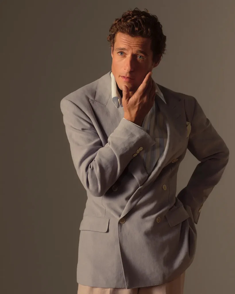 A male model in a contemplative pose with one hand to his chin, wearing a periwinkle Dunhill double-breasted blazer