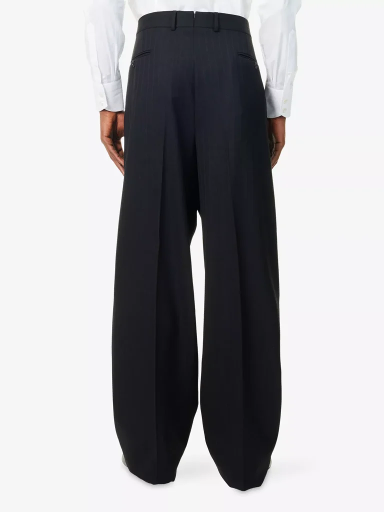 Back view of a male model wearing Tom Ford black pleated wide-leg wool trousers styled with a tucked-in crisp white dress shirt.